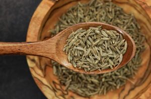 Detailed image of cumin seeds on a wooden spoon for culinary use.