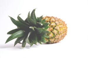 A single ripe pineapple with vibrant green leaves set against a white background, showcasing freshness.