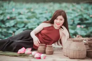A young woman poses gracefully amidst baskets and lotus flowers in a serene garden setting.