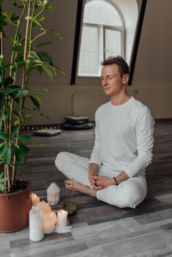 Man practicing meditation indoors surrounded by calming candles and plants.