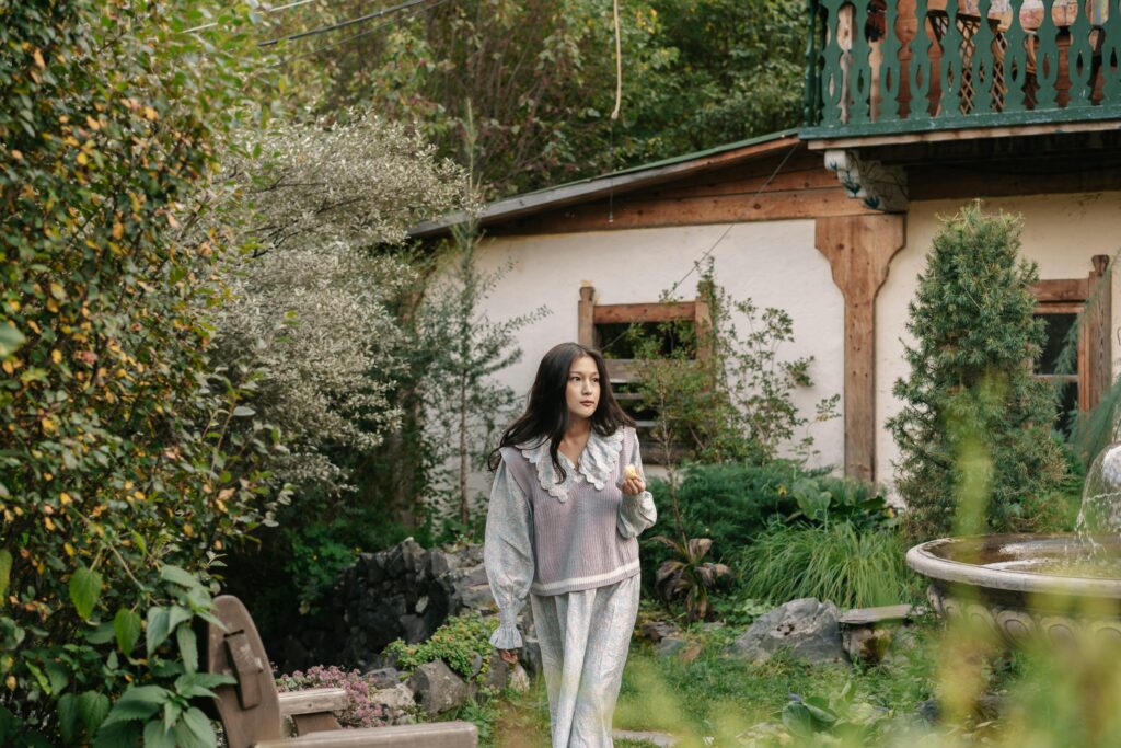 A stylish young woman walks through a lush garden with a vintage touch, radiating beauty and tranquility.